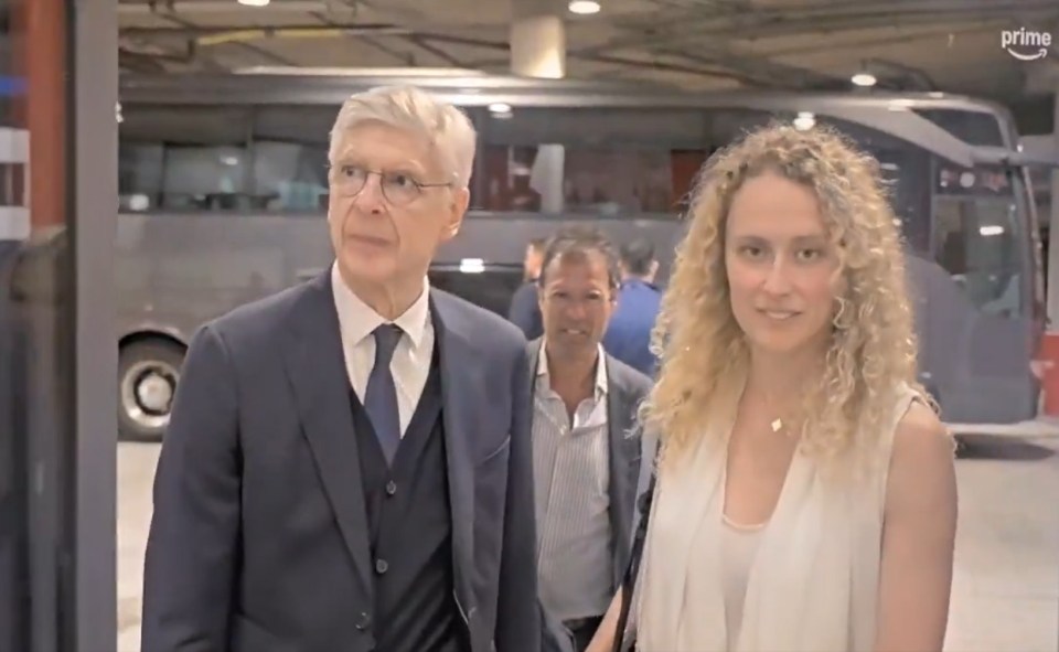 Arsene Wenger and a woman walking near a bus.