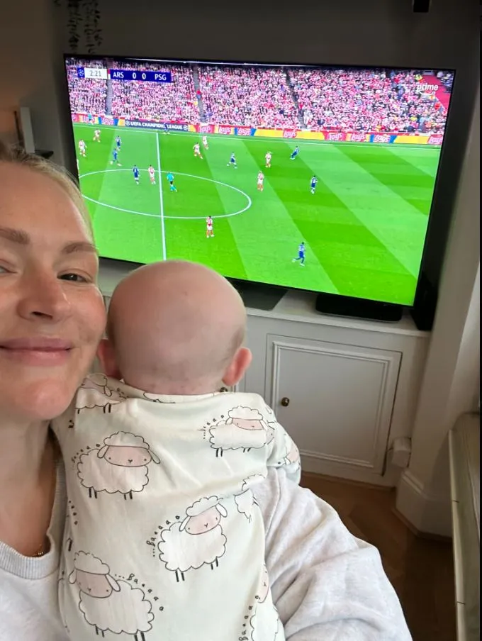 Woman holding baby while watching soccer game on TV.