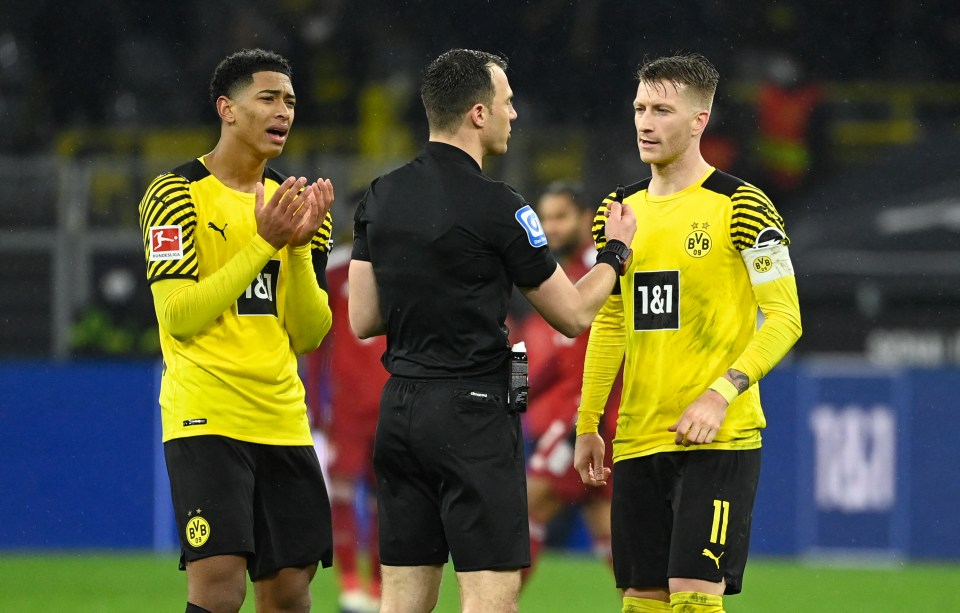 a referee shakes hands with two soccer players wearing yellow jerseys that say 1 & 1