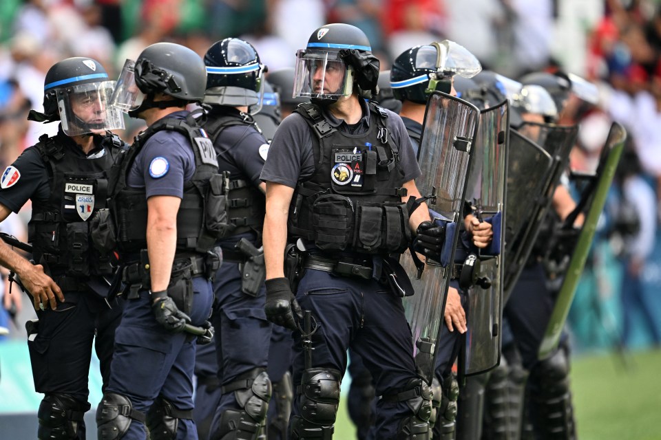 Riot police officers in full gear stand guard.