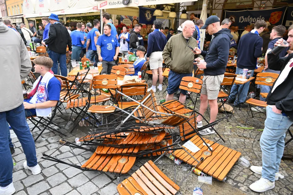 Overturned outdoor cafe chairs and tables amidst a crowd of people.