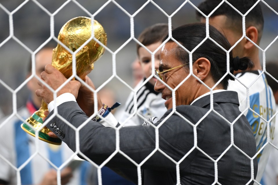 A man holds the FIFA World Cup trophy behind a net.